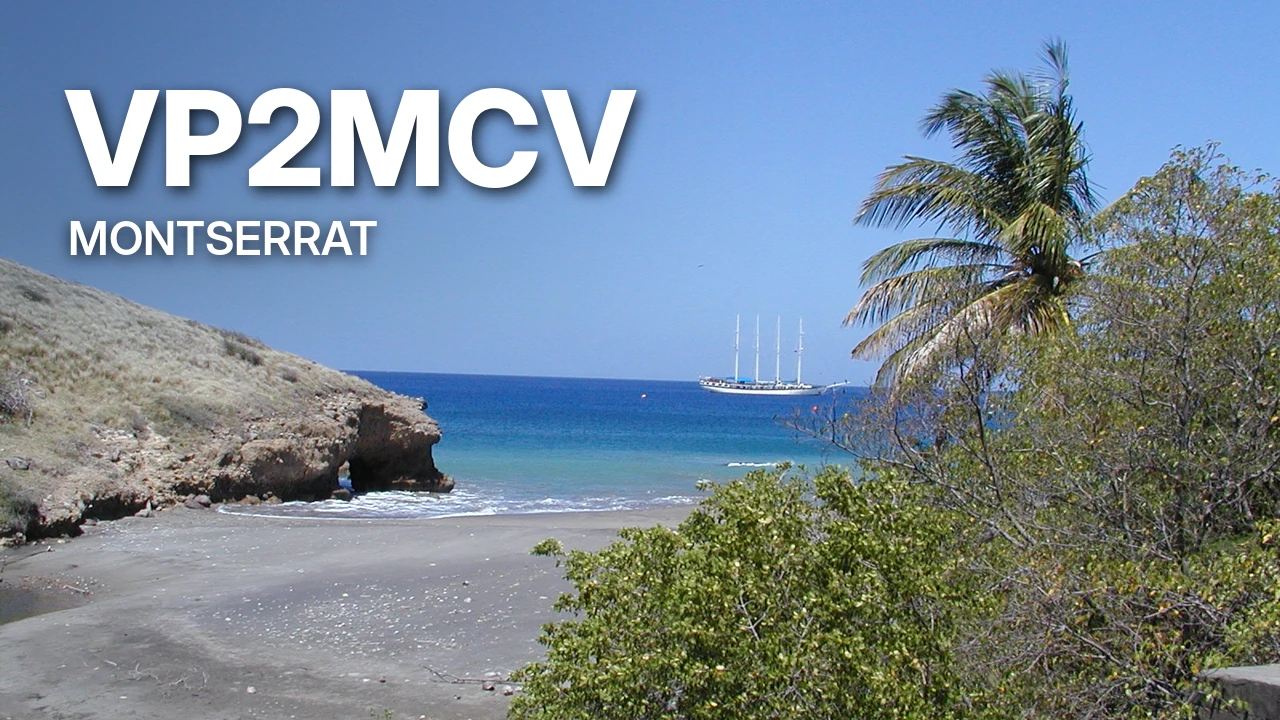 Пляж с тёмным песком, пальма и парусник в море, надпись VP2MCV Montserrat